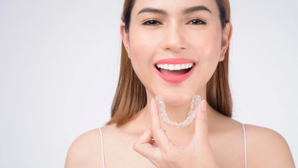 A woman holds up an Invisalign aligner close to her mouth after treatment in San Tan Valley.